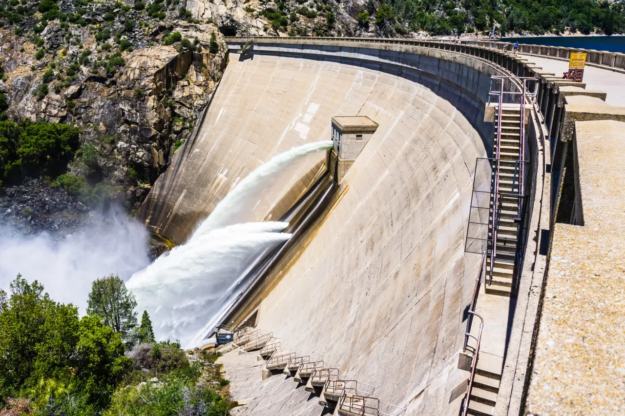 Concrete arch dam releasing water over its spillway, inspected under hydraulic structures supervision